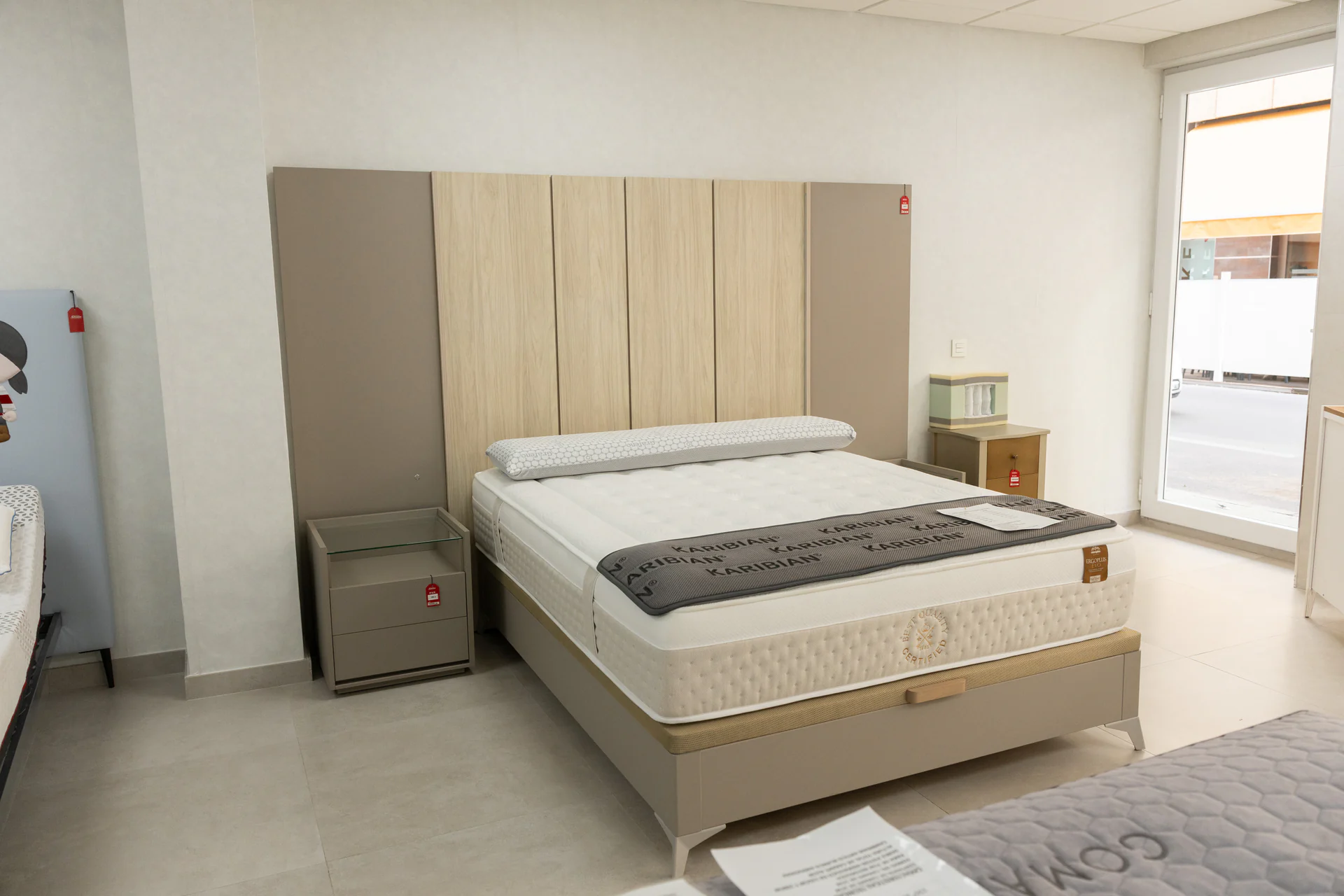 Dormitorio de exposición con cama, cabecero y mesitas en Muebles Amate